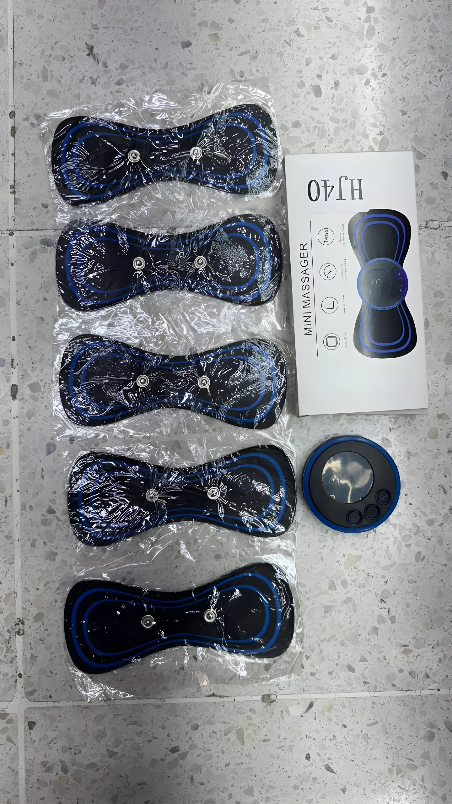 Masajeadora mini con 5 electrodos tipo mariposa en empaque transparente, caja de producto "HJ40 MINI MASSAGER" al lado.