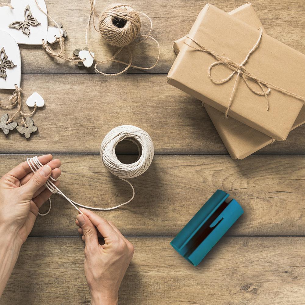 Cortador de papel regalo azul turquesa, sobre madera, con cuerdas y cajas de regalo.