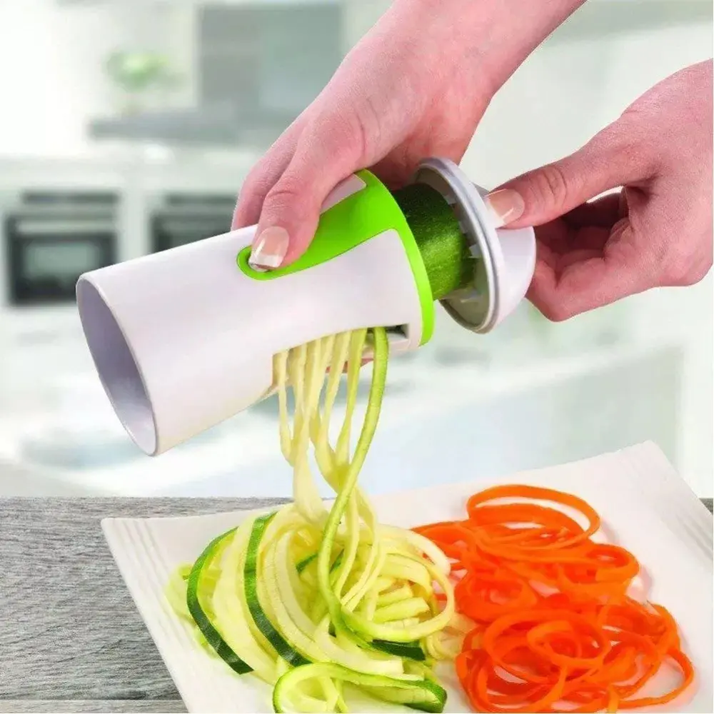 Cortador en espiral blanco y verde para hacer fideos de calabacín y zanahoria sobre plato blanco.