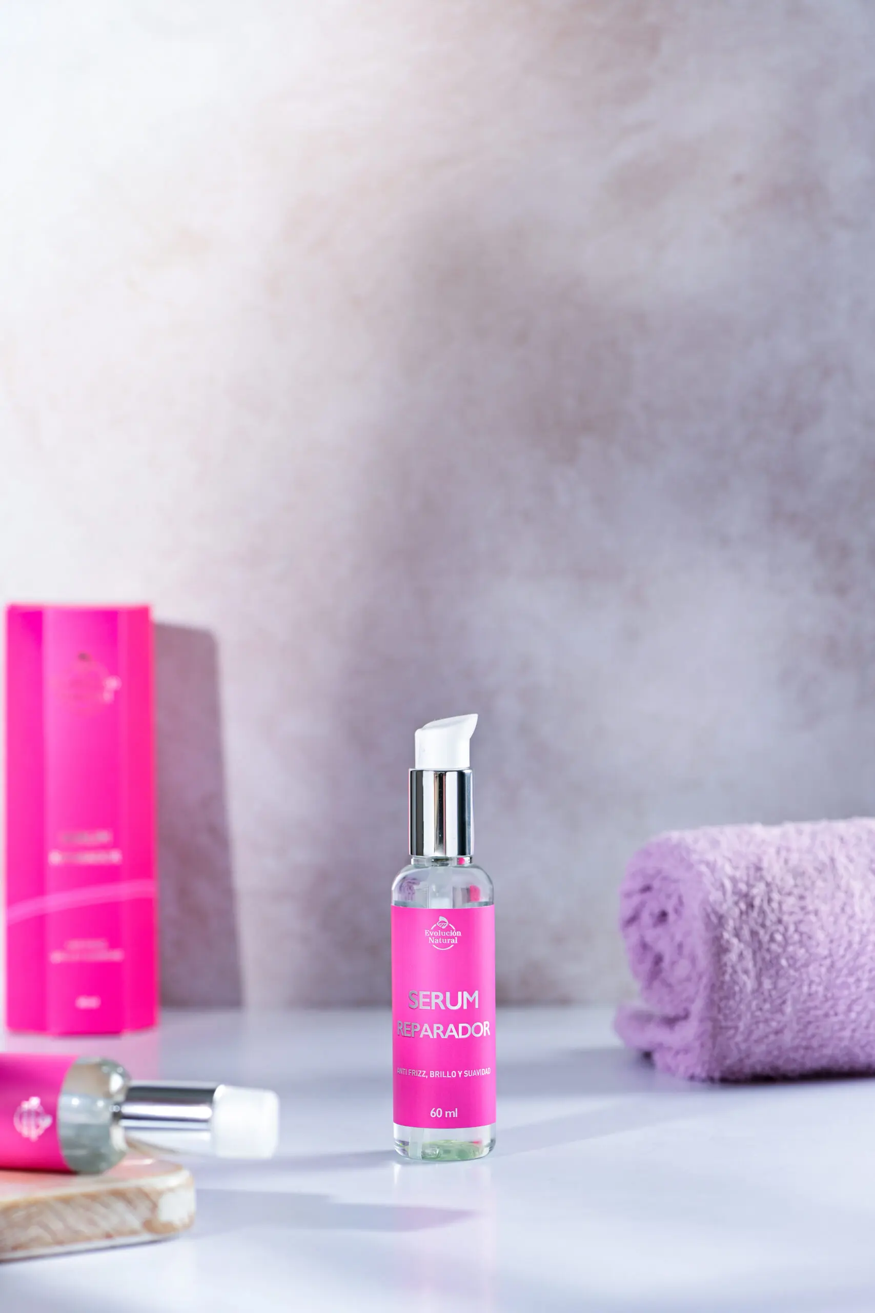 Serum reparador capilar en frasco transparente con etiqueta fucsia, 60 ml, junto a toalla lila.