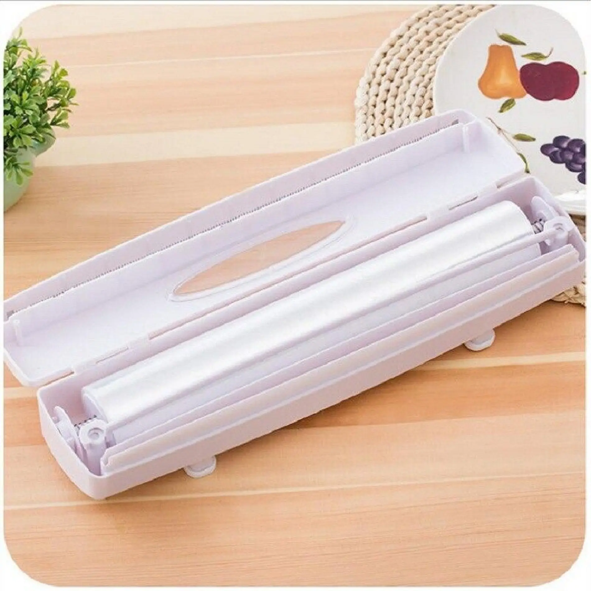 Dispensador de film y aluminio blanco con tapa abierta, mostrando el mecanismo de corte y el rollo interno, sobre una superficie de madera.