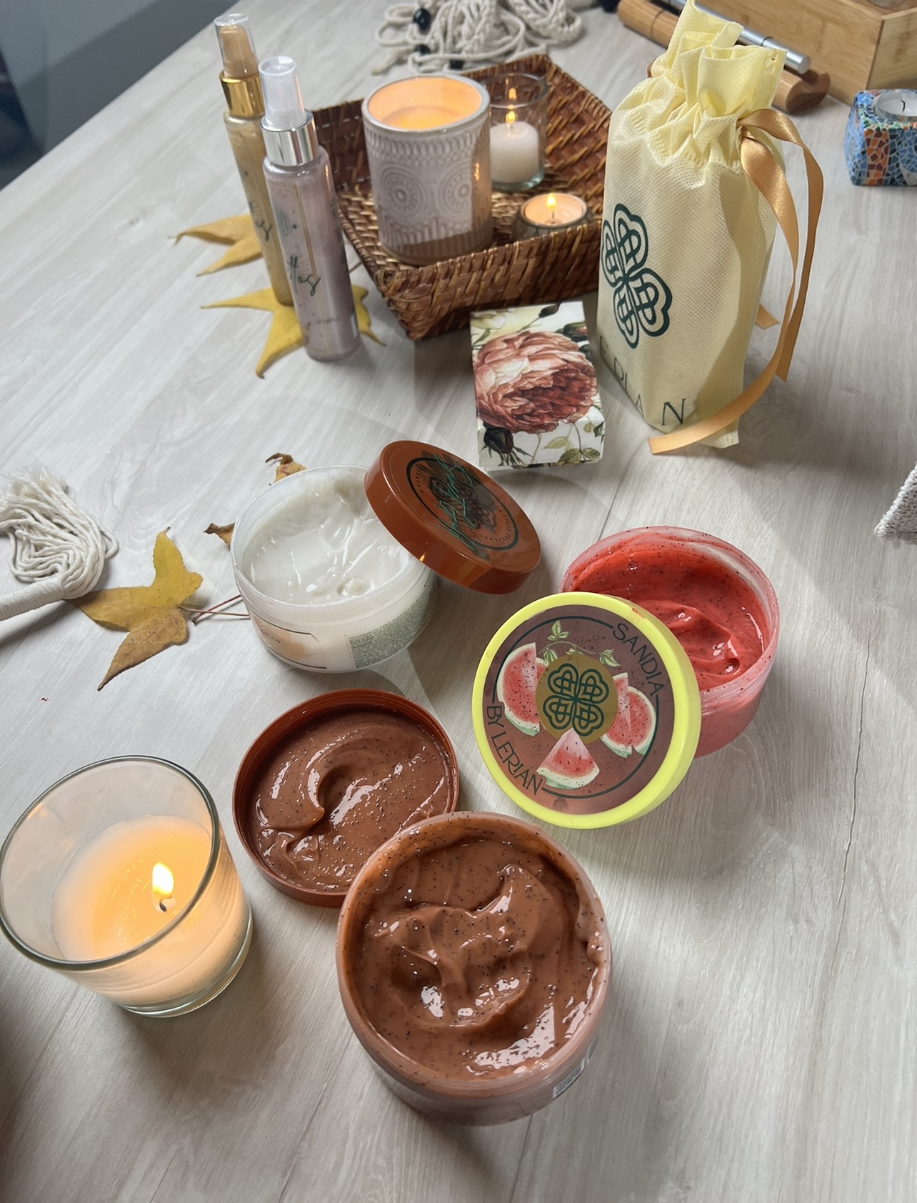 Set de exfoliantes por LERIAN en Cocoa y Sandia, acompañado de velas, jabones y botellas, sobre mesa de madera.