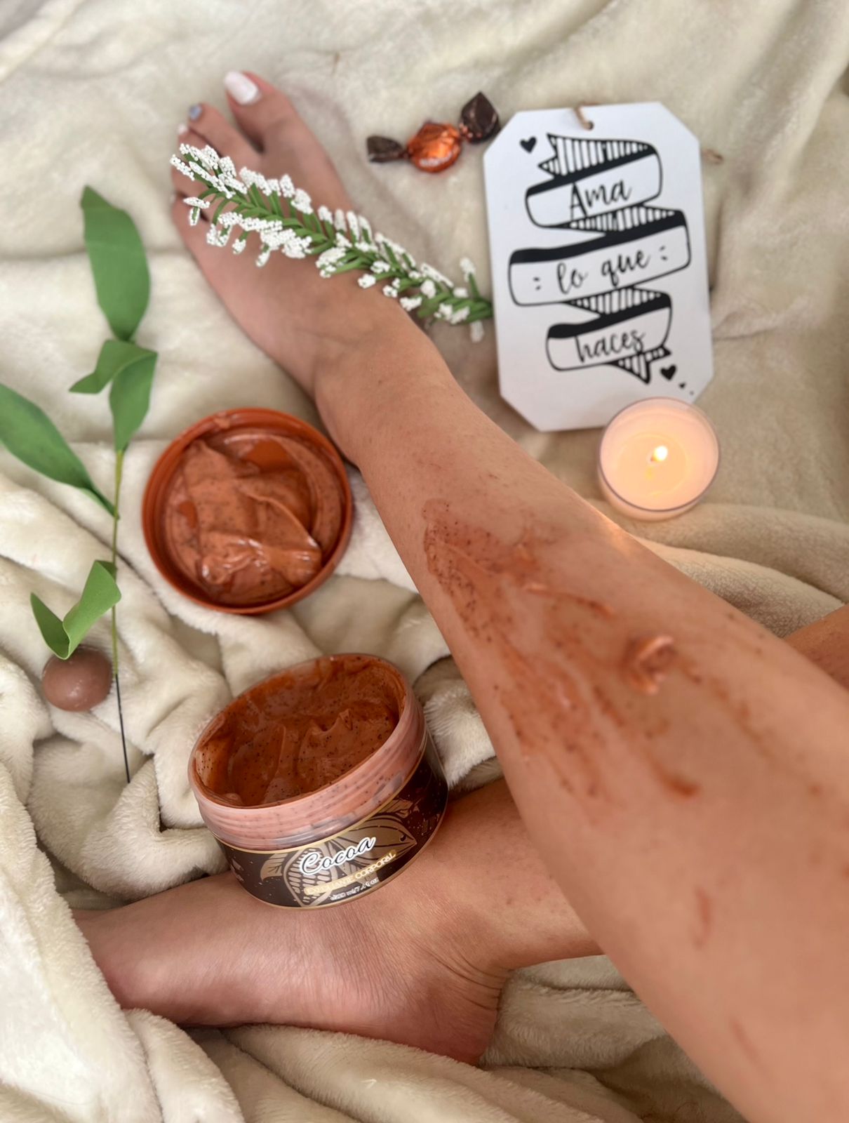 Set de 2 exfoliantes corporales de Cocoa aplicados en la pierna, rodeado de elementos de spa y dulce.
