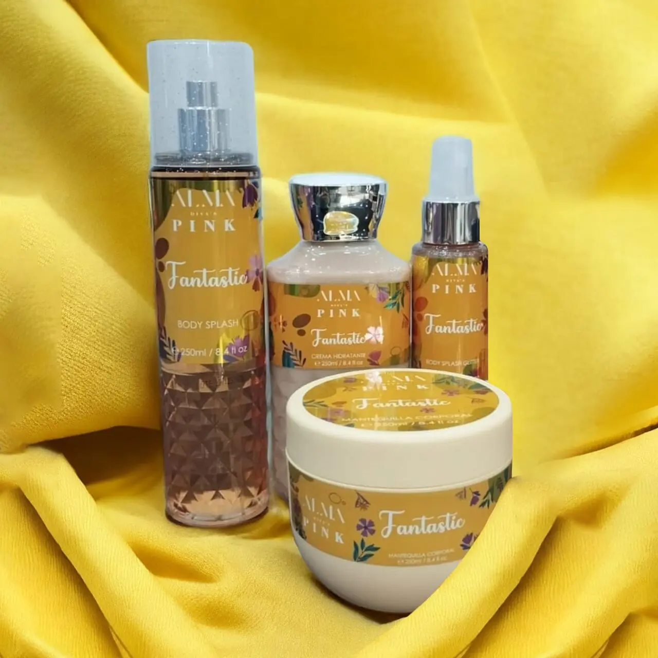 Set de 4 productos Alma Divas Pink: body splash, crema hidratante y body splash glitter, en envases dorados y amarillos sobre tela.
