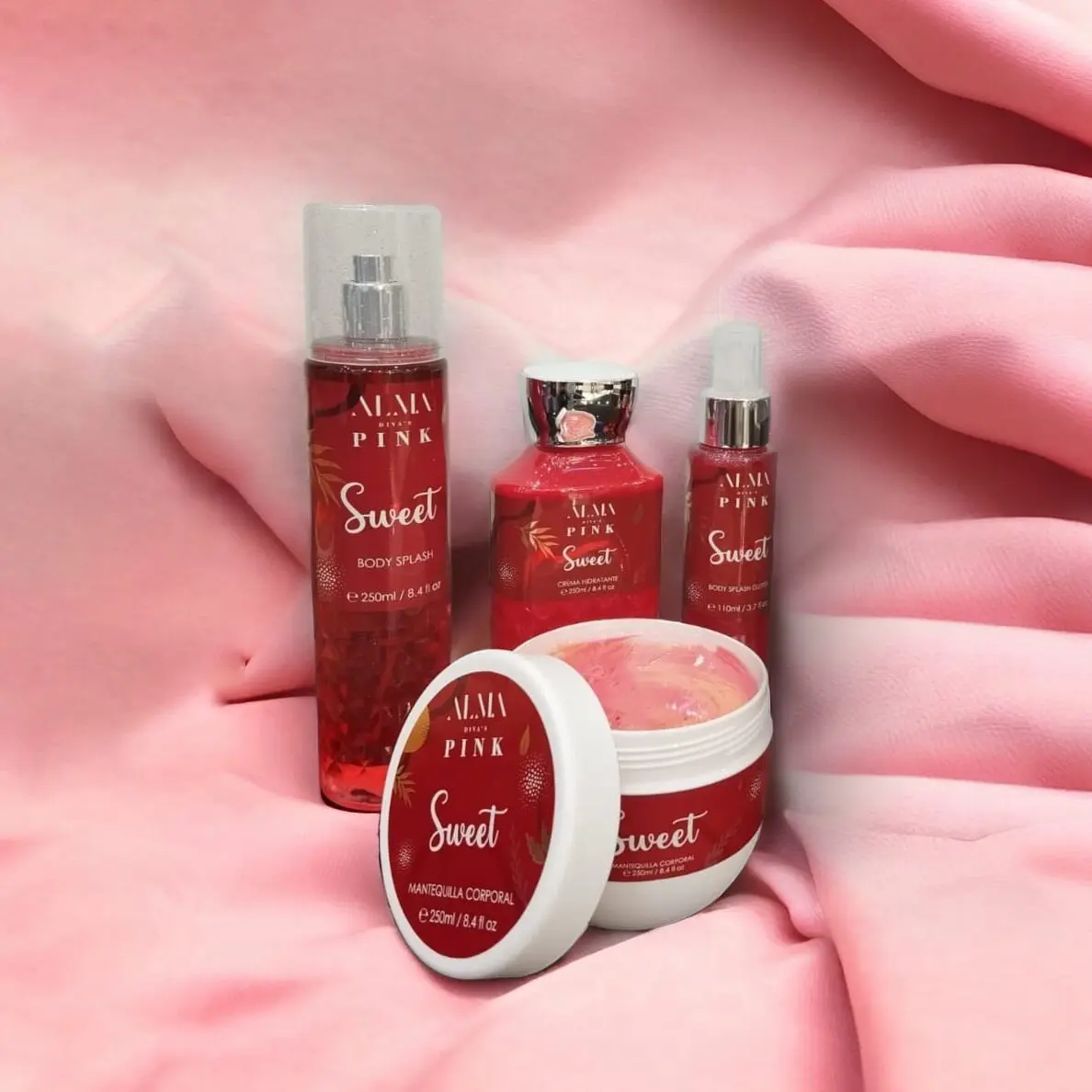 Set de 4 productos Alma Divas Pink: body splash, crema hidratante y manteca corporal en envases rojos con detalles dorados sobre tela rosa.