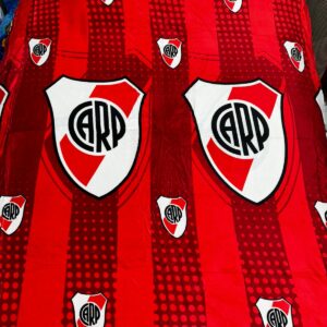 Cobija deportiva roja con escudo de River Plate repetido, textura suave, diseño a rayas y puntos.