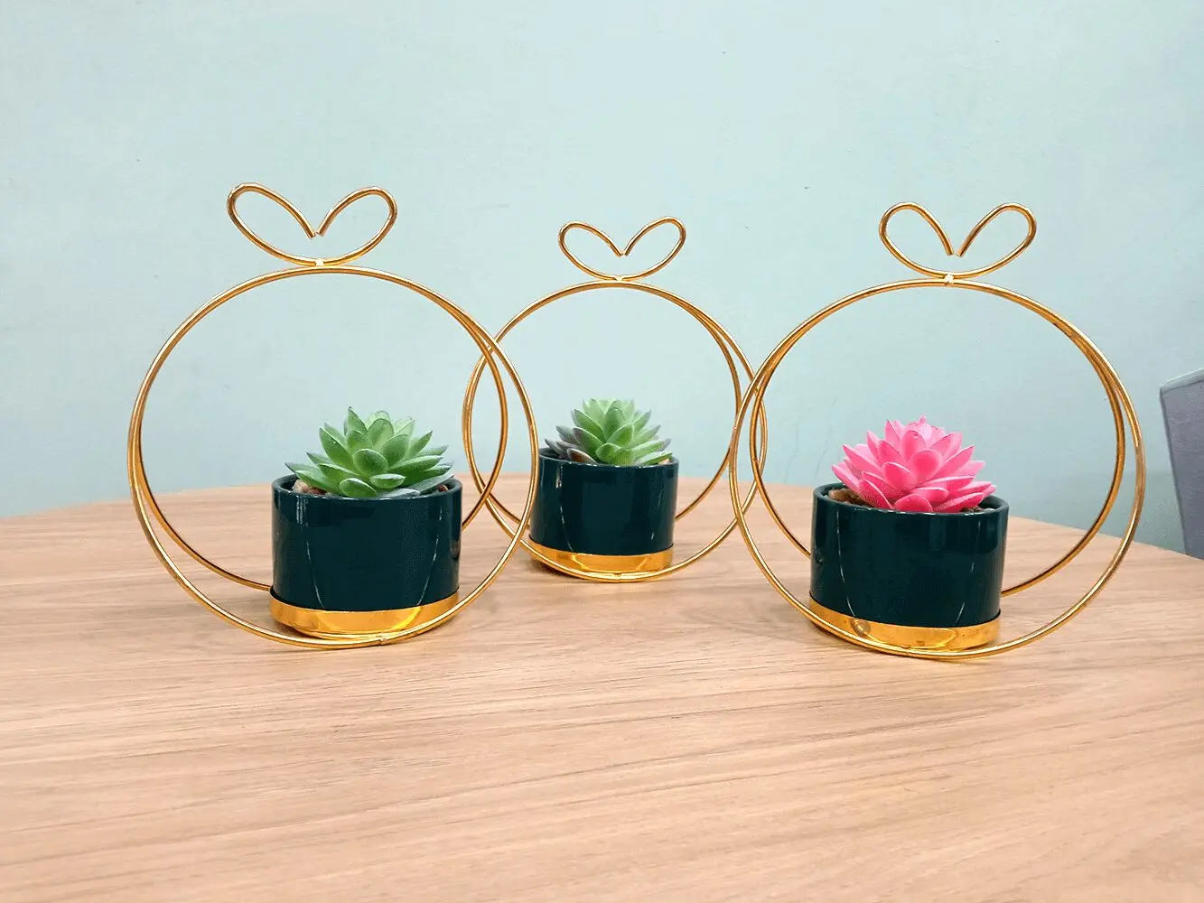 Trío de suculentas artificiales en macetas verde oscuro con soporte dorado, ideal para decorar.