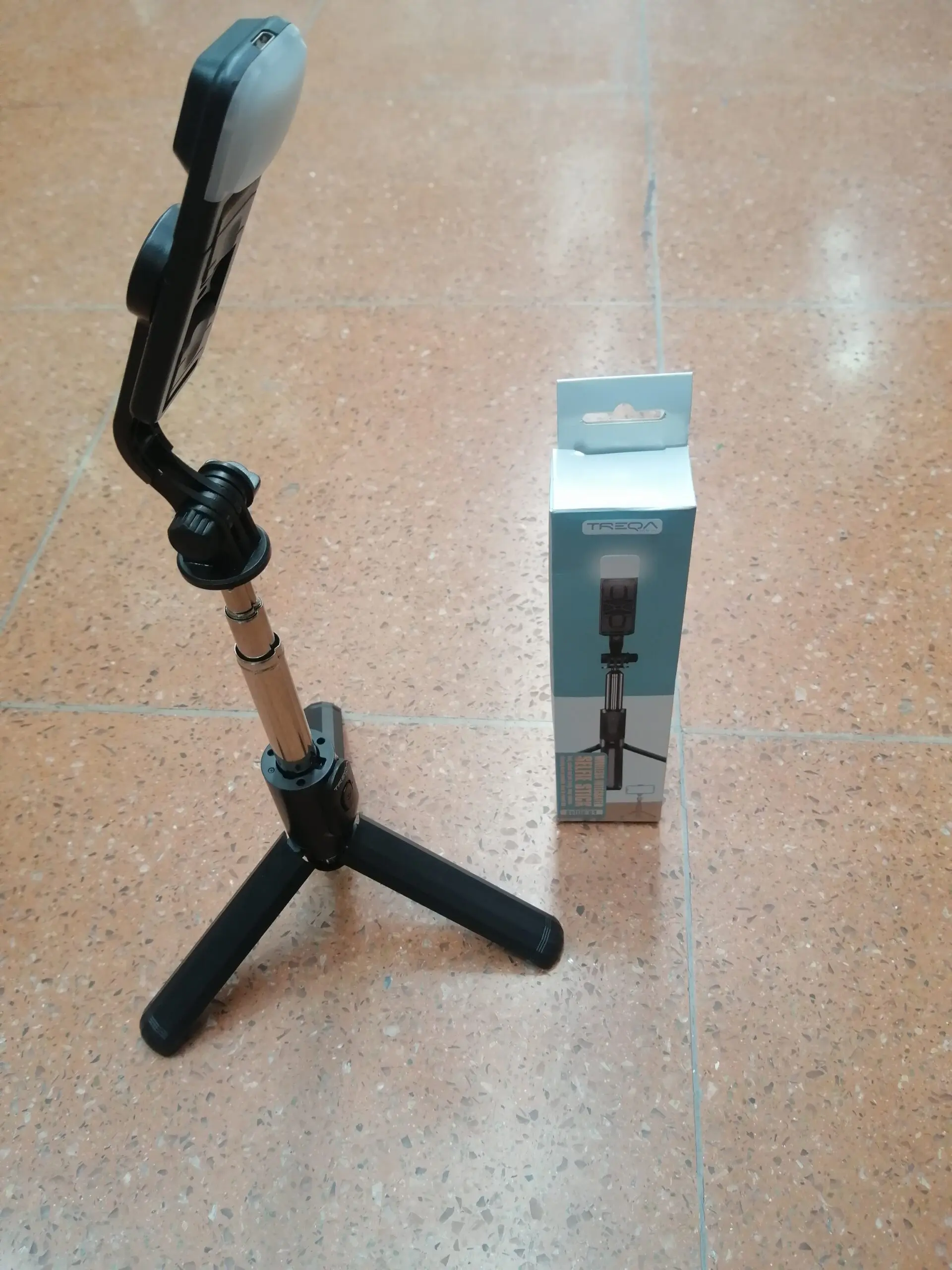 Trípode para celular con luz LED integrado, color negro, en caja azul.
