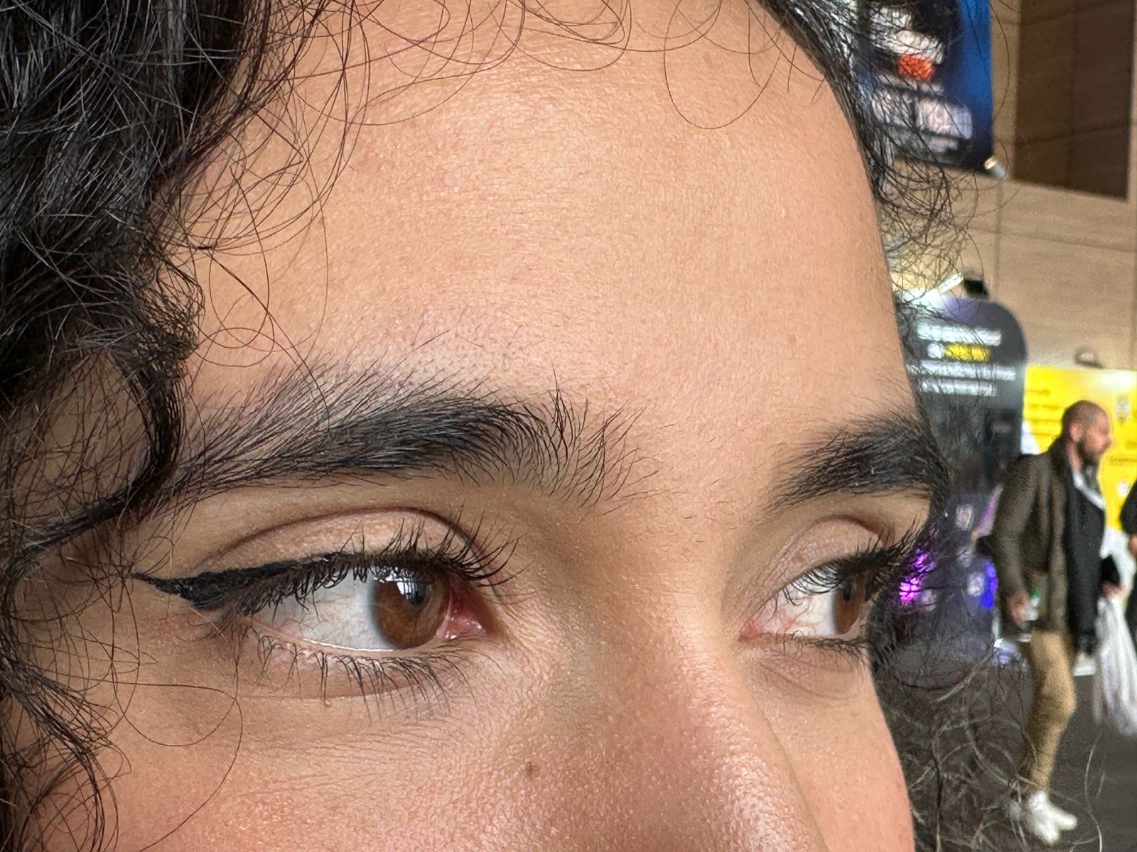 Primer plano de ojos con delineado cat eye, pestañas y cejas pobladas, cabello rizado oscuro.