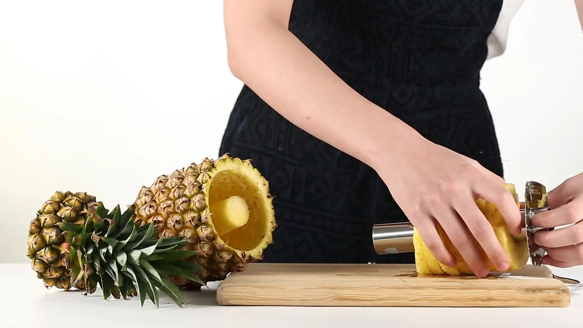 Pelador de piña cortando rodajas de piña amarilla sobre tabla de madera.