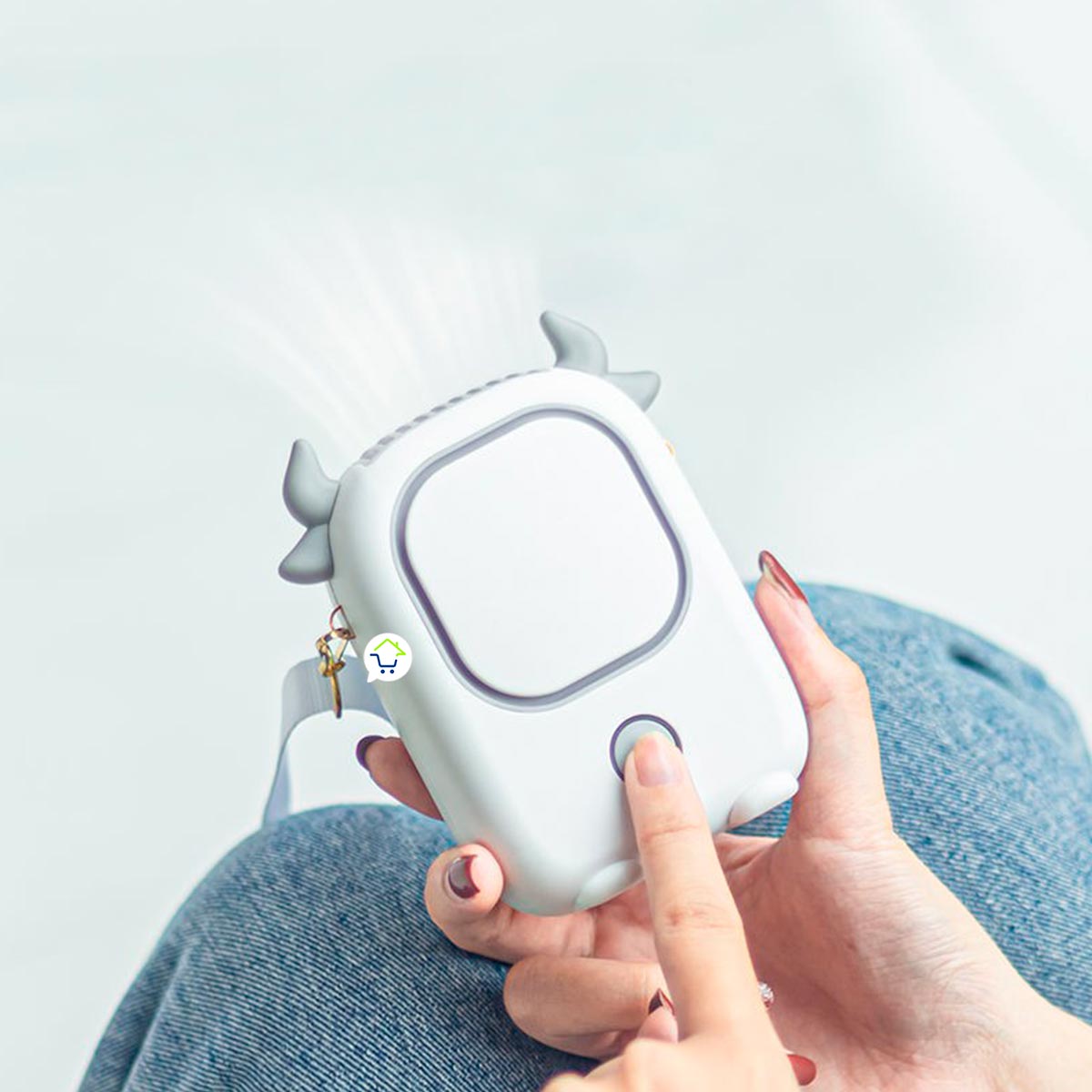 Ventilador de cuello blanco con diseño de vaca, sostenido por una mano, ideal para portar y refrescar.