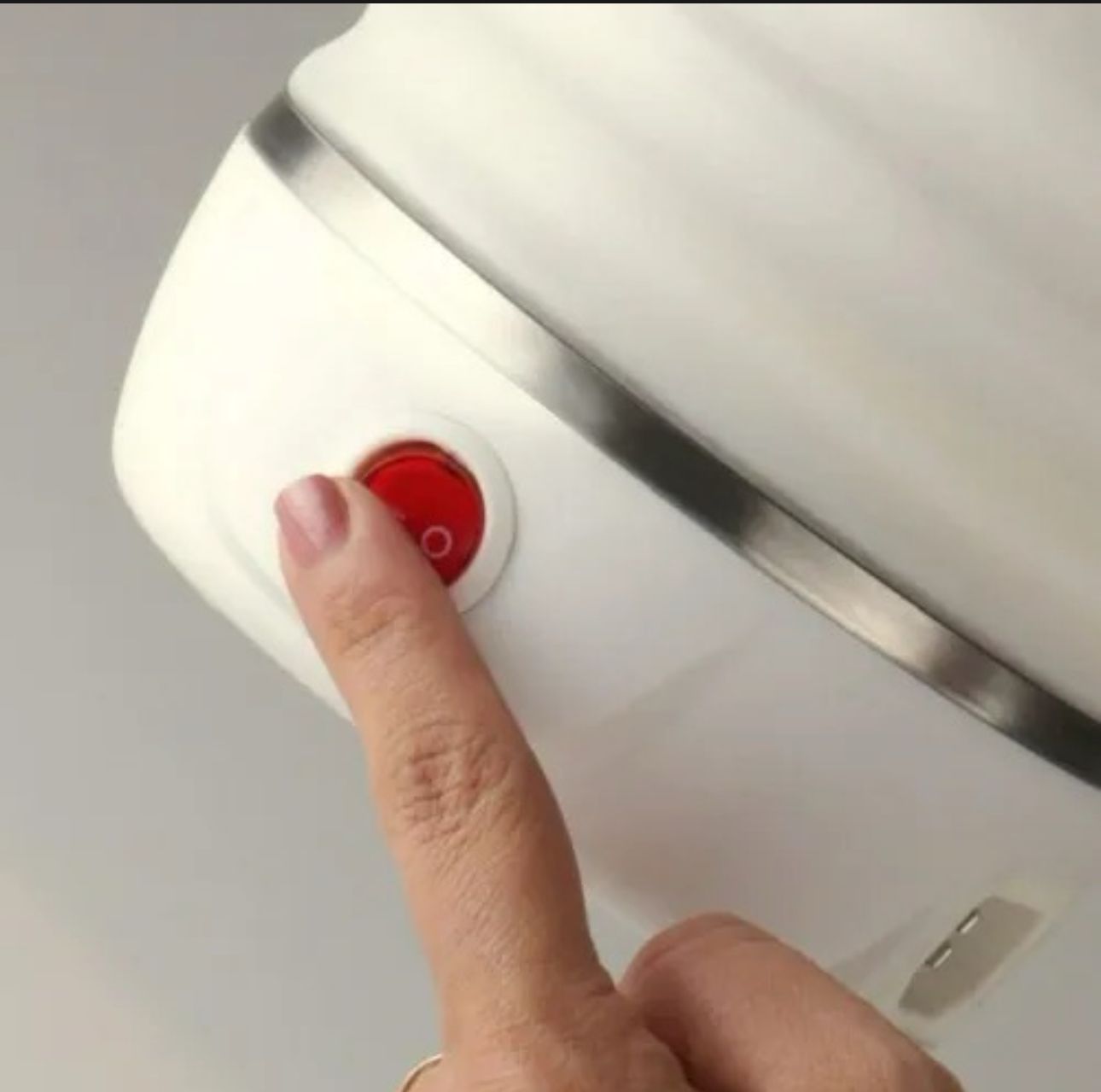 Primer plano de una jarra eléctrica de silicona blanca con base metálica, donde un dedo presiona el interruptor de encendido rojo en el costado.