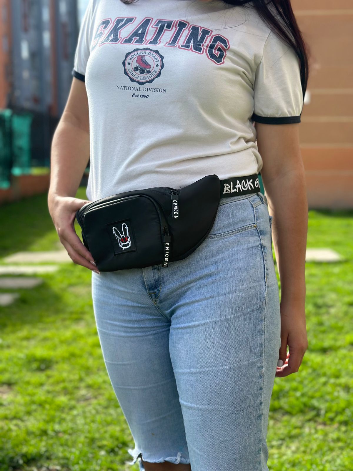 Riñonera negra impermeable unisex Goat con parche de conejo y correa "BLACK G" sobre jeans claros.
