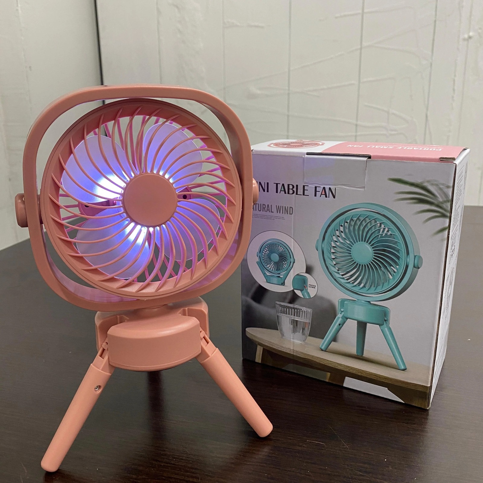 Mini ventilador recargable rosa con trípode, aspas iluminadas y caja del producto.