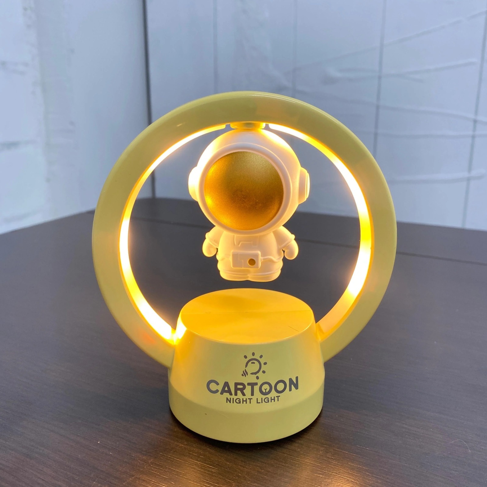 Lámpara de noche LED amarilla con astronauta flotante, diseño moderno para mesita.