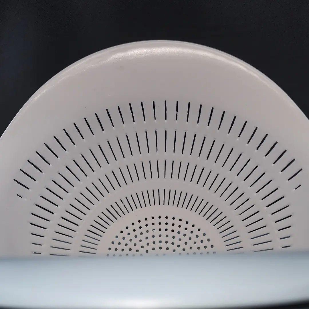 Colador blanco de plástico con perforaciones lineales y circulares.