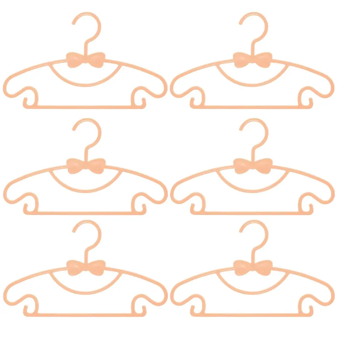 Seis ganchos para ropa de bebé color salmón con forma de moño, ideales para colgar y organizar prendas.