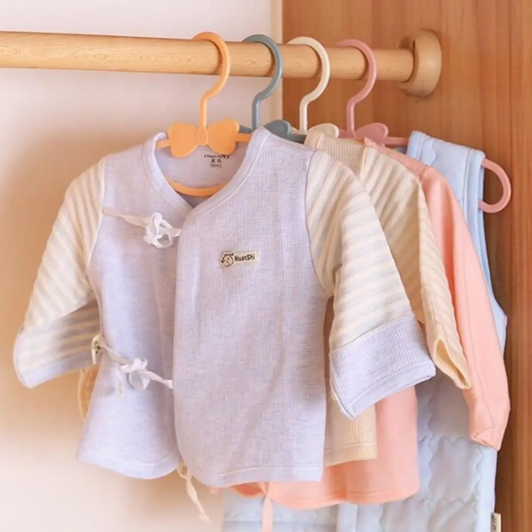 Ganchos flexibles para ropa de bebé en tonos pastel, organizados en un tendedero de madera.