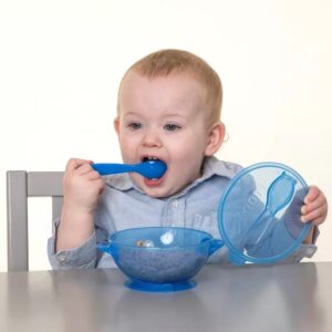 Bebé azul comiendo cereal con cuchara de un plato antiderrame con ventosa y tapa.
