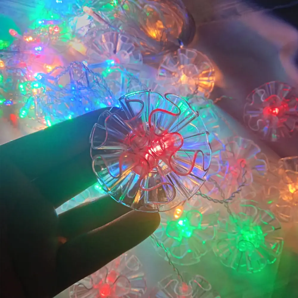 Cortina de luces LED navideñas con 3 metros, decorada con flores transparentes y luces de colores variados, sostenida por una mano.