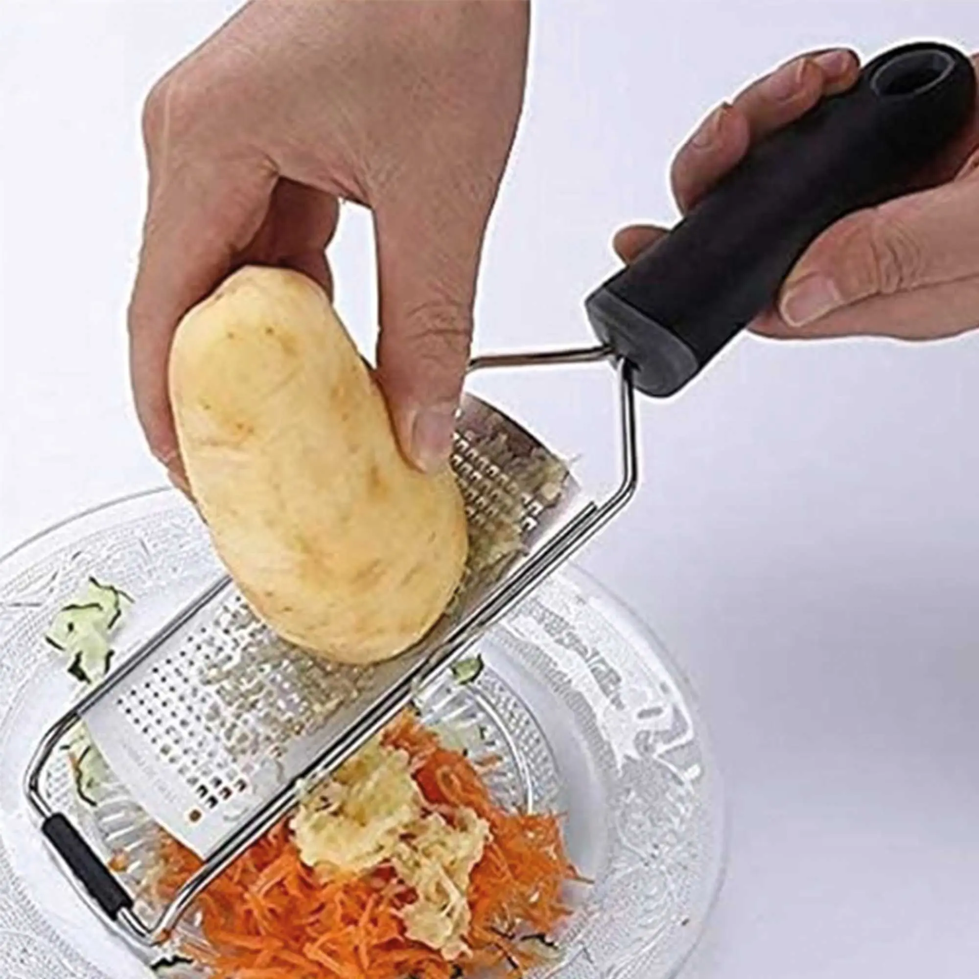 Rallador de acero inoxidable con mango ergonómico negro, rallando papa sobre zanahoria en un plato.