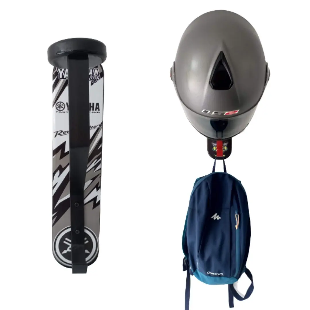 Portacasco mural Yamaha de un puesto. Soporte vertical blanco con estampado negro. Muestra un casco gris mate colgado en el gancho superior y una mochila azul en el inferior.