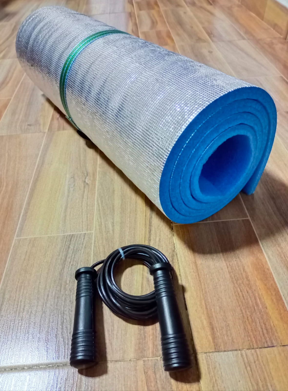 Colchoneta de ejercicio plateada y azul enrollada junto a un lazo negro con mangos acanalados.