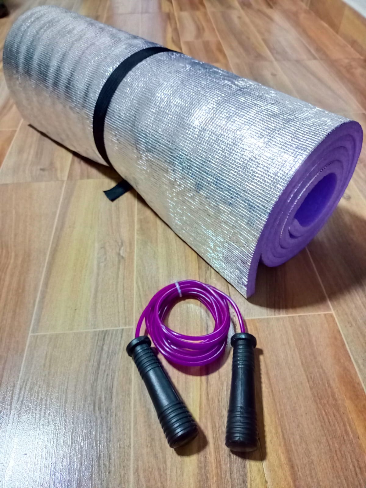 Colchoneta plateada enrollada con lazo morado, ideal para ejercicios en casa o al aire libre.