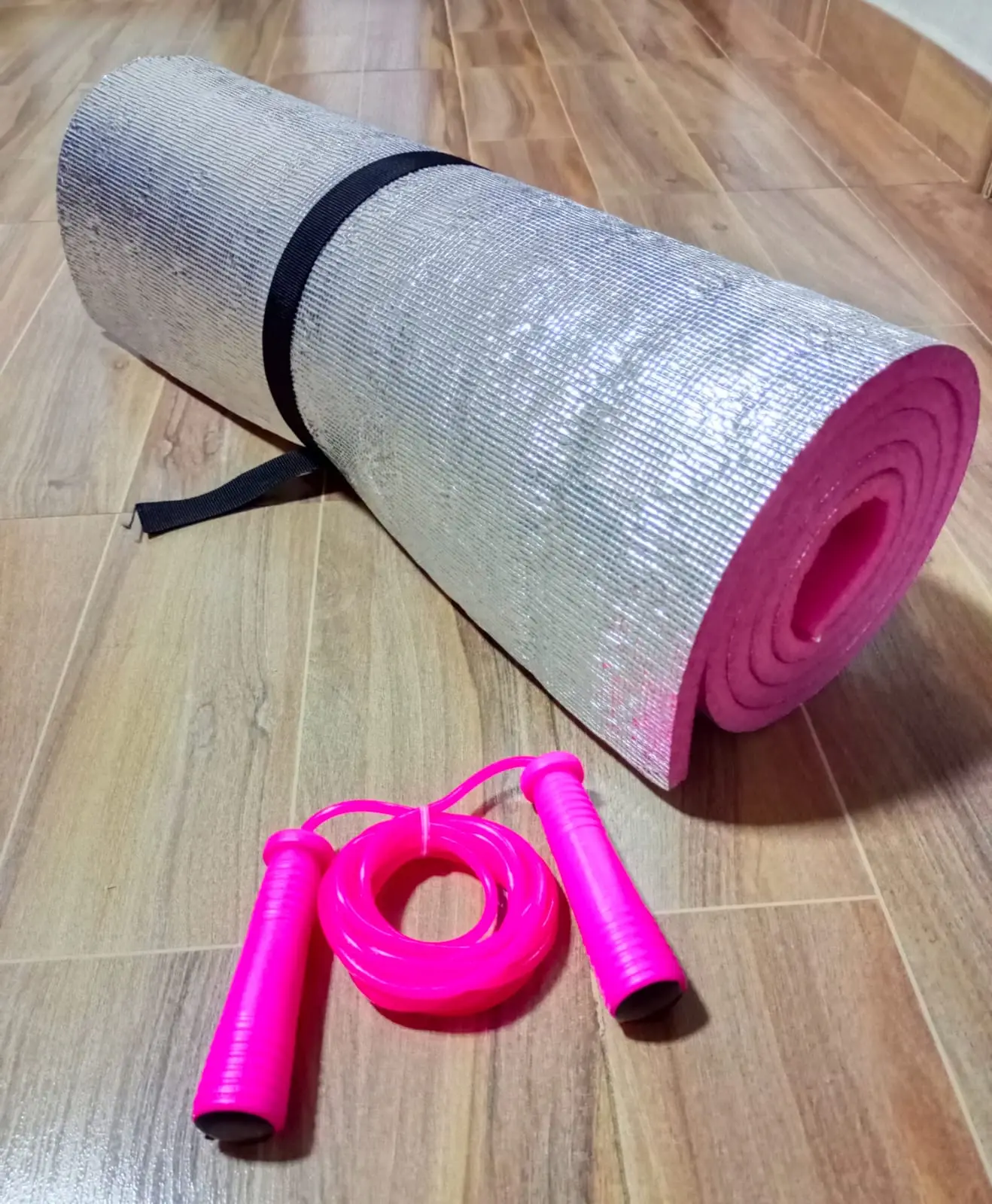 Colchoneta plateada enrollada con lazo rosado en el suelo de madera.