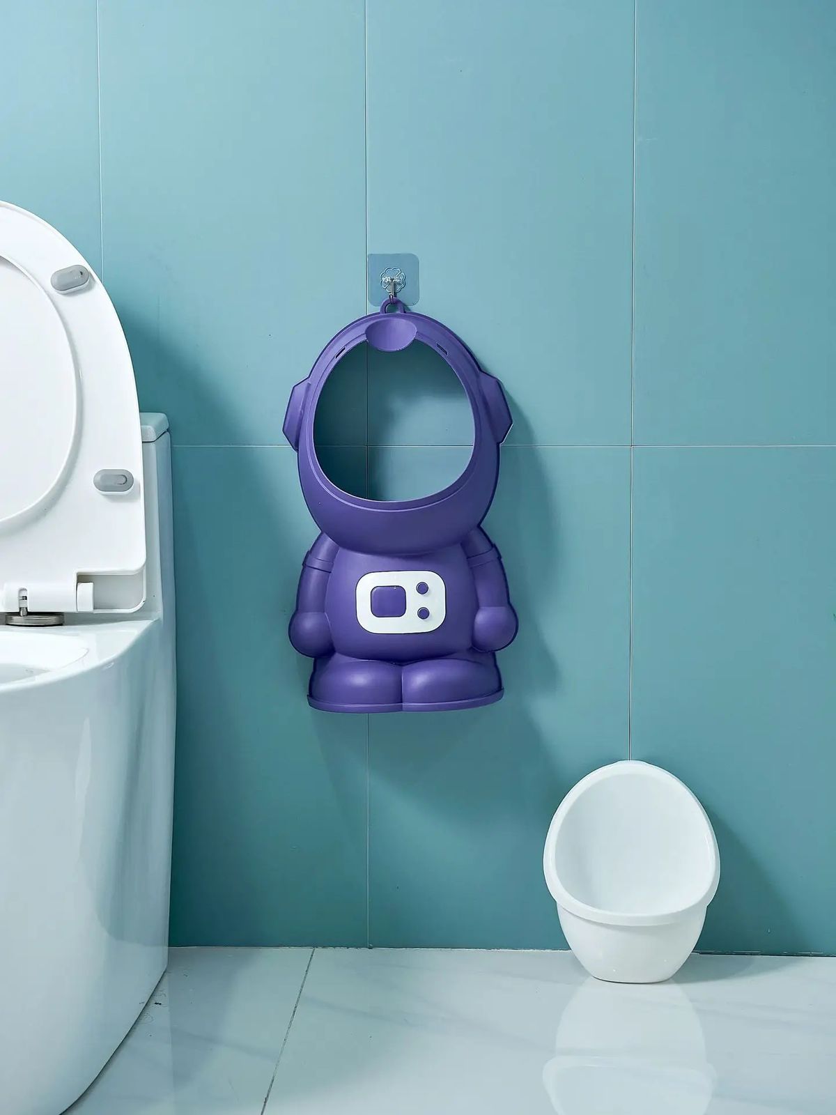 Orinal infantil morado diseño astronauta, colgado en pared azul junto a inodoro blanco.