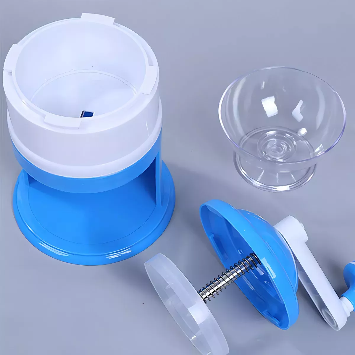 Triturador de hielo manual azul y blanco con manivela, recipiente transparente y bol pequeño.