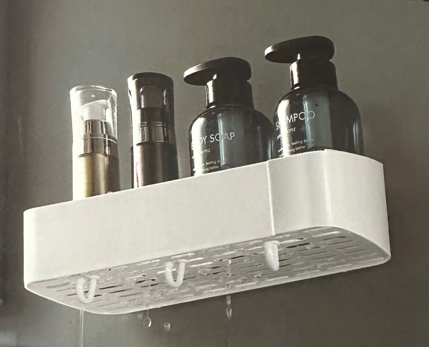 Repisa lineal blanca para baño con dispensadores de jabón y champú, escurre agua.
