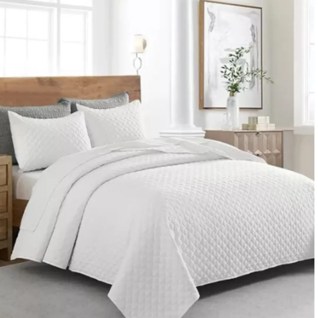 Colcha española blanca acolchada doble faz, vista de cerca en cama con almohadas a juego.