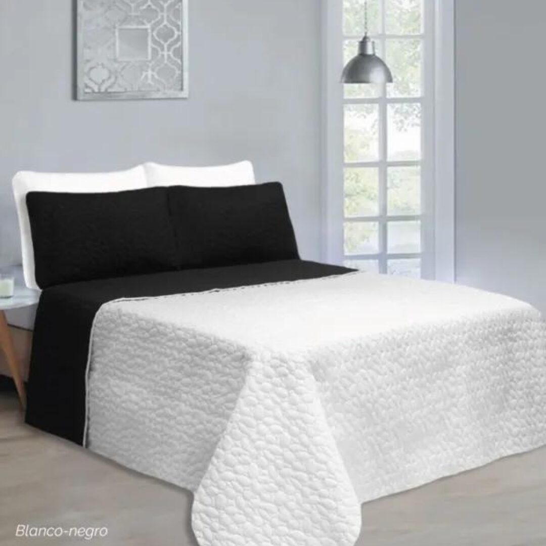 Colcha española doble faz blanco con patrón texturizado y almohadas negras, vista frontal.