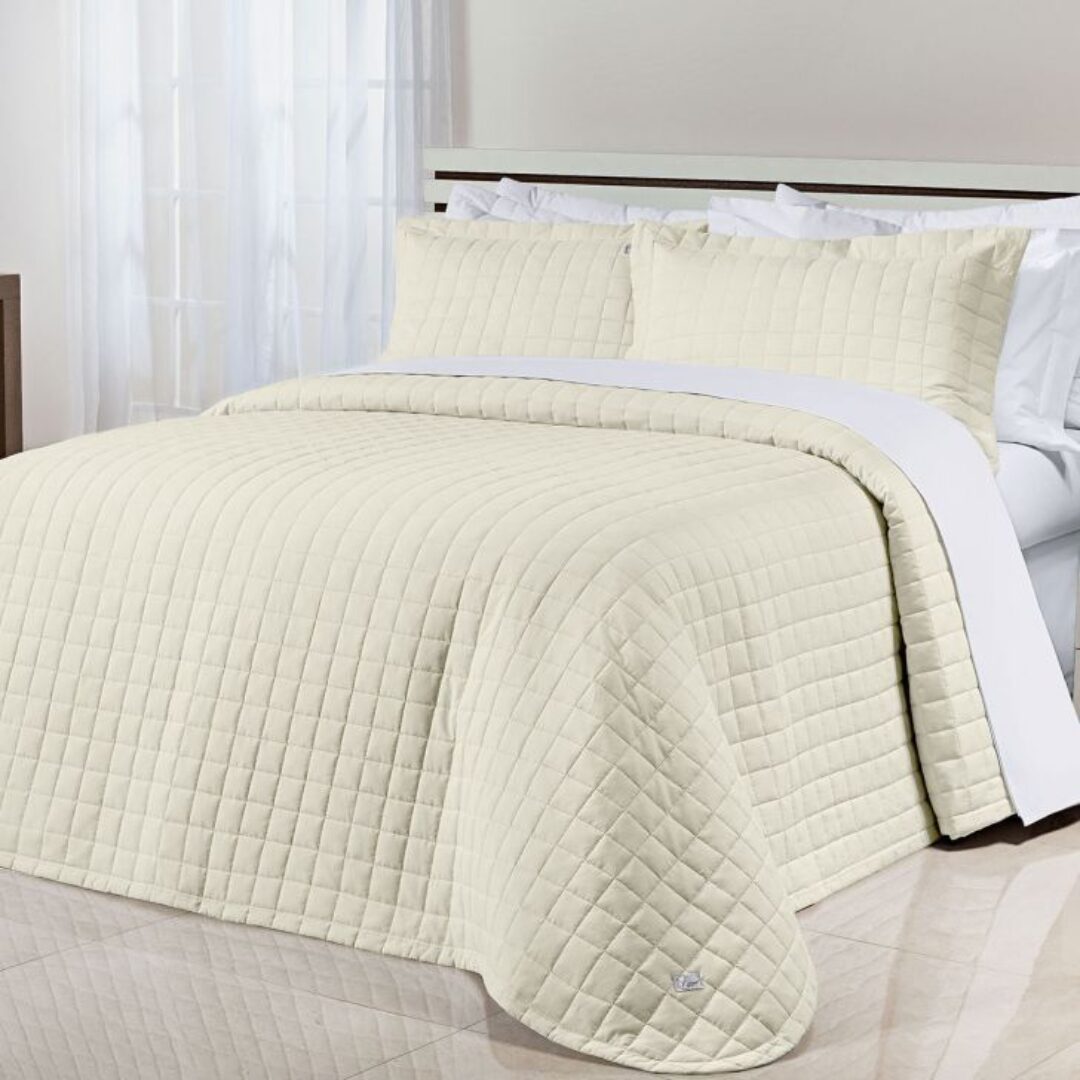 Colcha española doble faz, color marfil, textura acolchada, con cojines a juego sobre cama, para dormitorio.