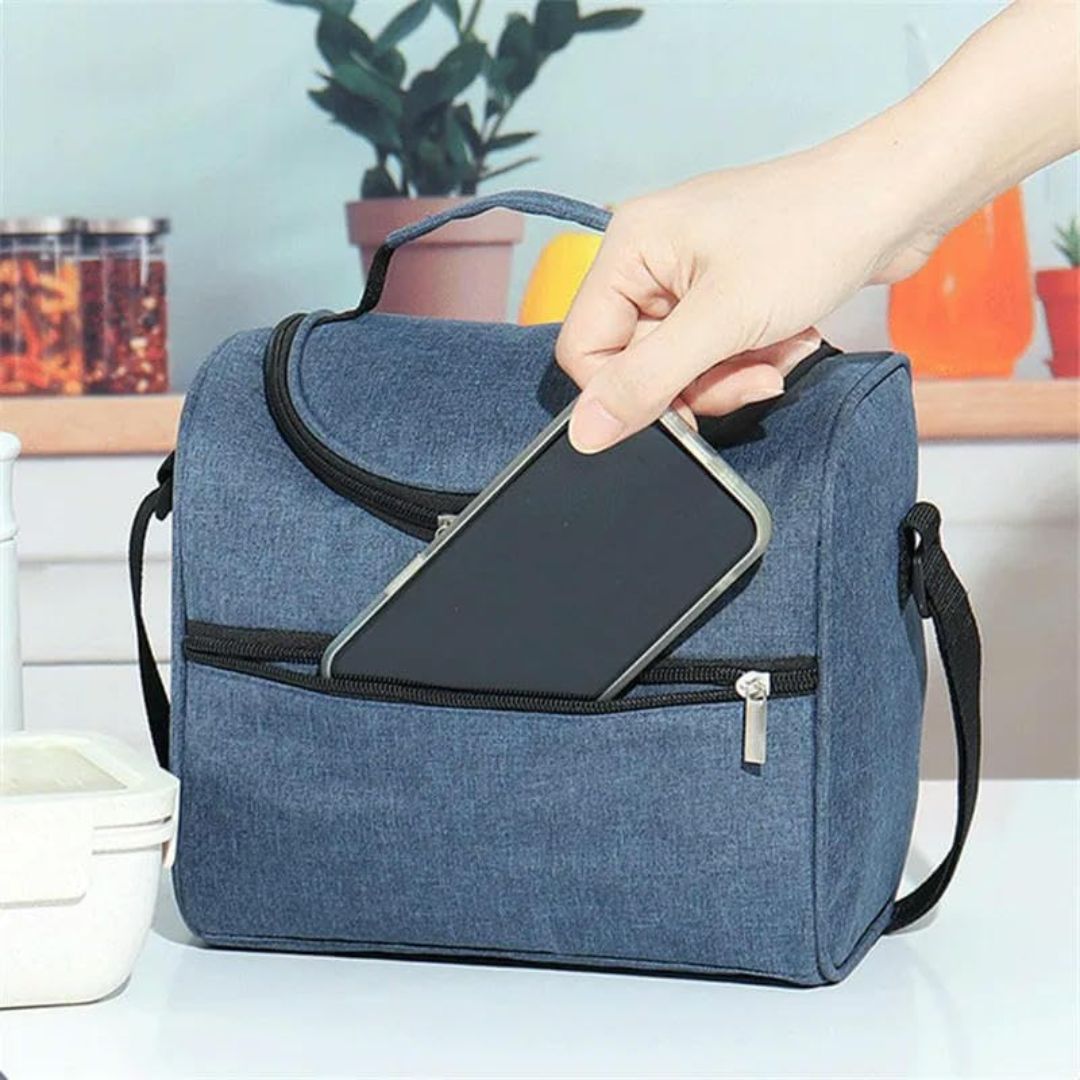 Lonchera térmica azul de tela con bolsillo frontal, mano inserta smartphone.