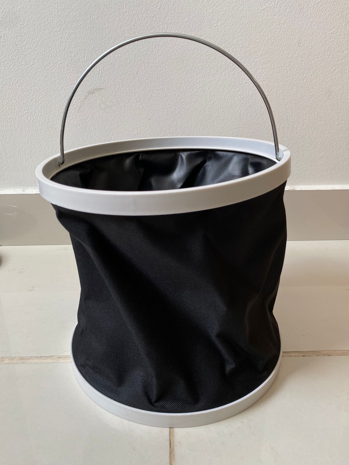 Balde plegable negro de tela con aro blanco y asa metálica, para agua.
