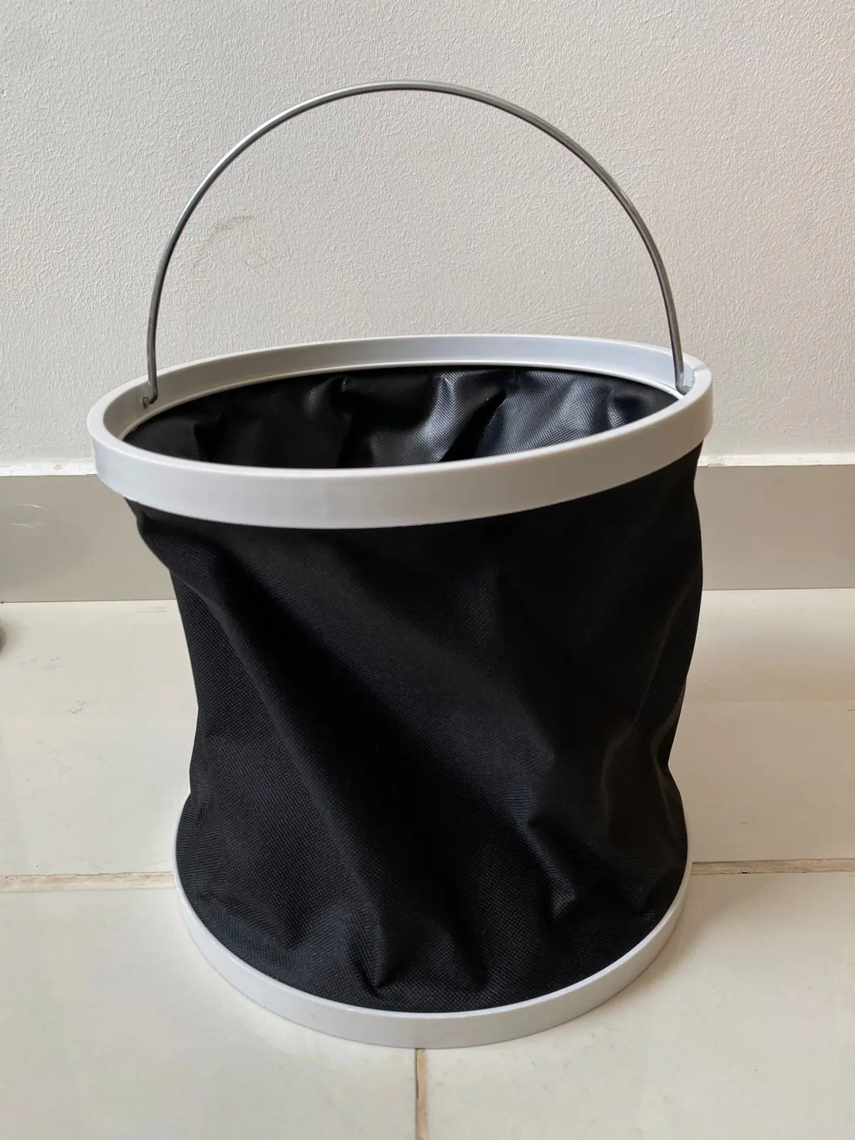 Balde plegable negro de tela con aro blanco y asa metálica, para agua.