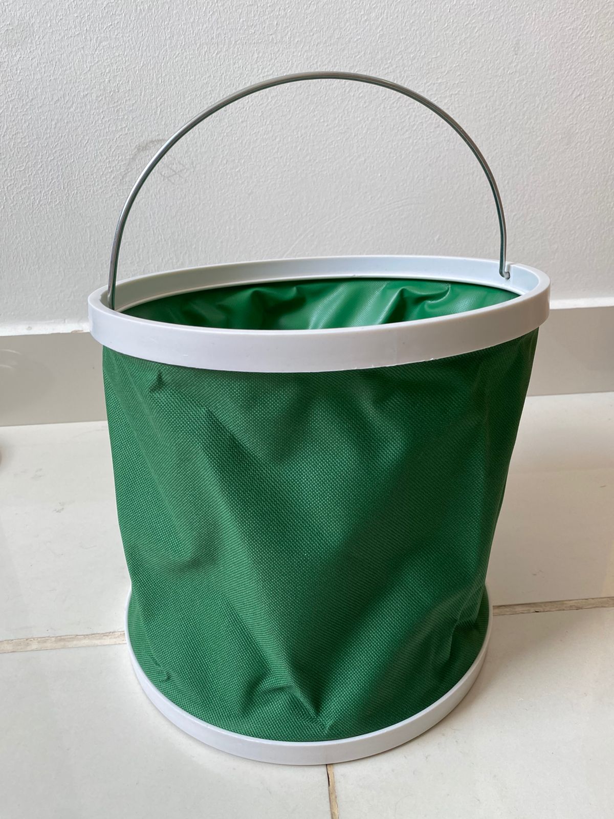 Balde plegable verde con asa metálica y borde blanco, ideal para camping y pesca.