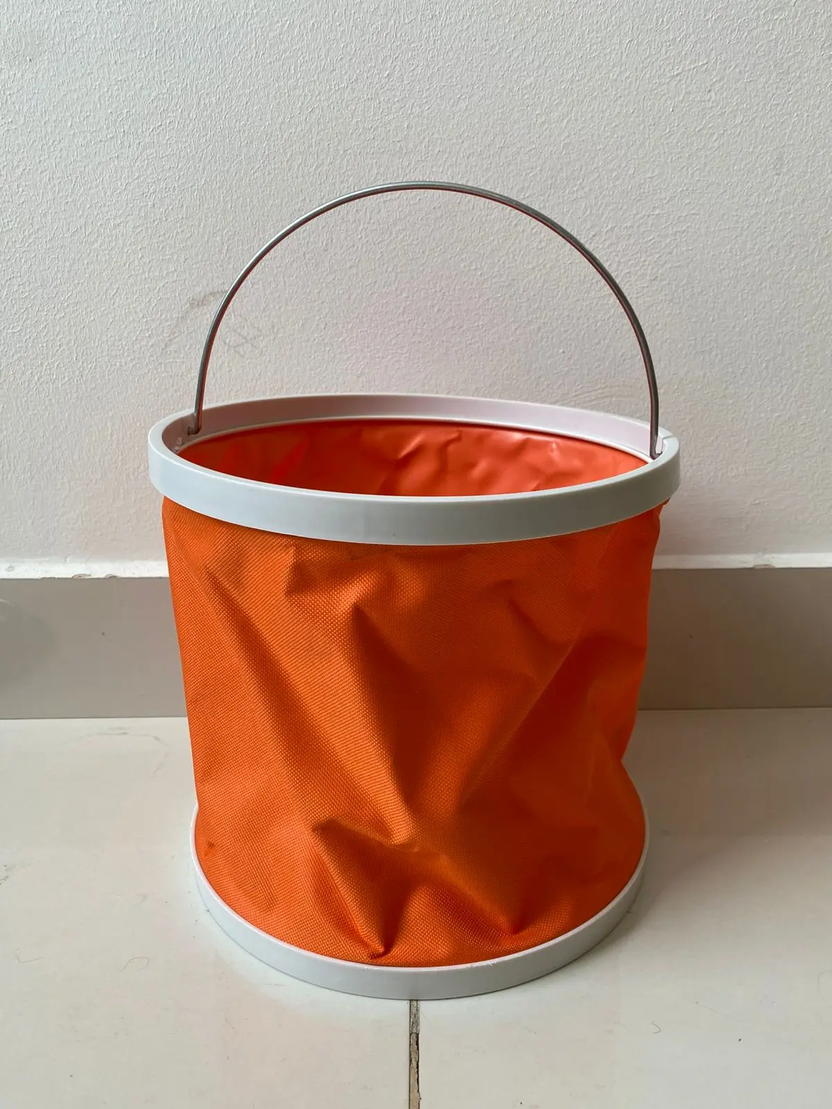Balde plegable naranja de tela impermeable con aro blanco y asa metálica, ideal para actividades al aire libre.
