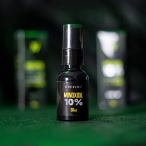 Botella oscura con spray de Minoxidil 10% Crexion 30ml, fondo verde y negro, ideal para crecimiento capilar.