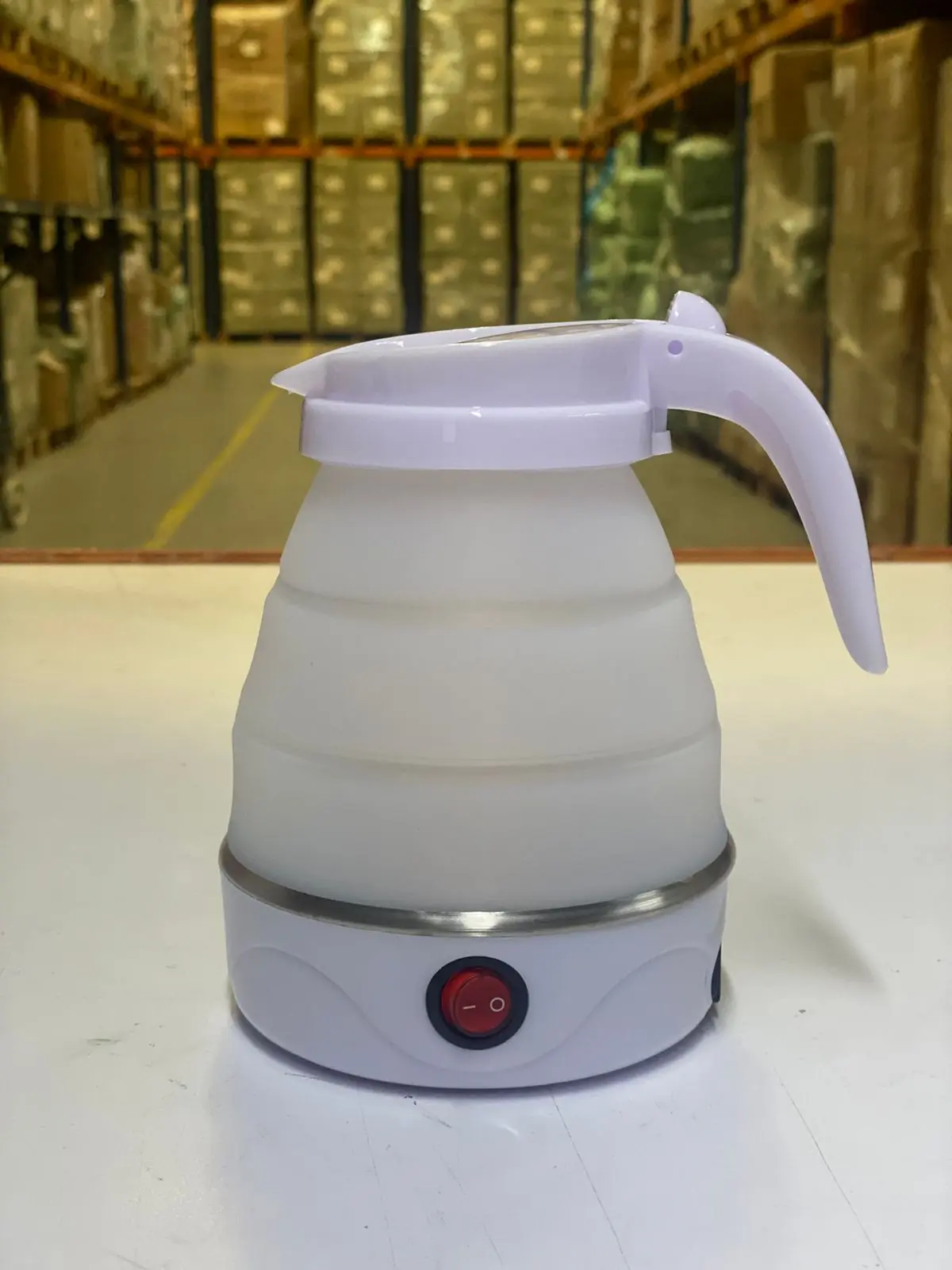 Hervidor de agua portátil blanco de silicona plegable con asa y botón de encendido.