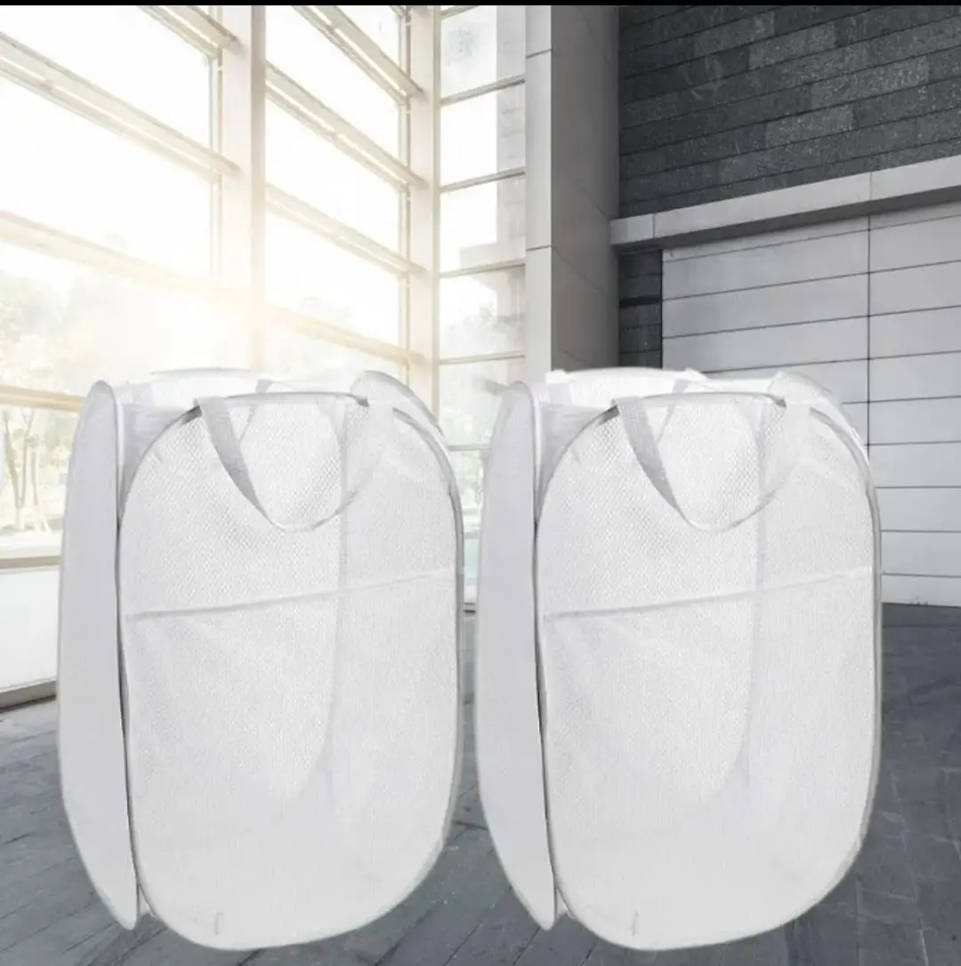 Dos canastas de ropa blancas plegables de malla, con asas, en interior moderno.