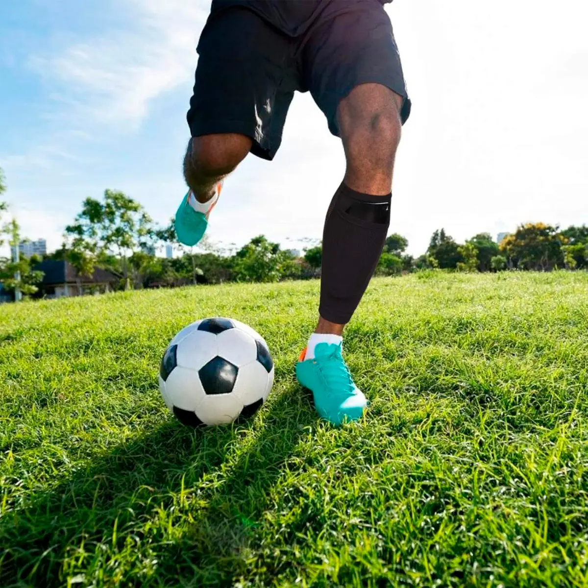 Media deportiva negra 25cm para futbolista pateando balón en césped.