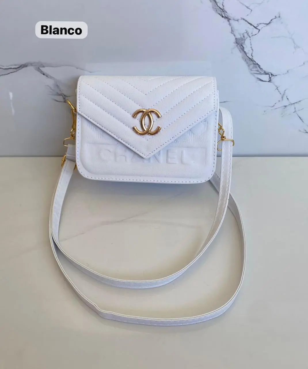 Cartera Chanel blanca con logo dorado y textura acolchada, estilo bandolera.