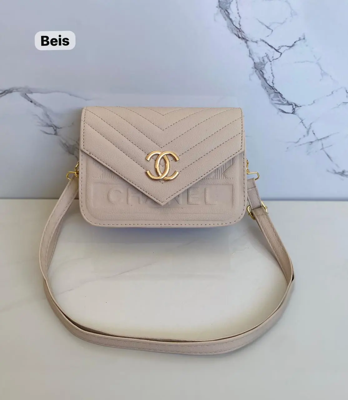 Cartera pequeña beige texturizada con logo dorado de Chanel y correa delgada, ideal para uso casual.
