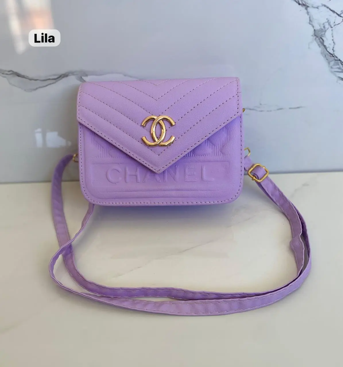 Cartera pequeña morada de cuero sintético con logo Chanel dorado y correa ajustable.