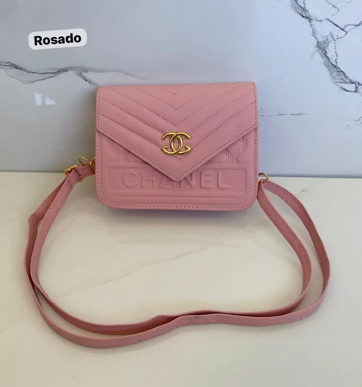 Cartera rosa pastel "Mani Chanel" con logo dorado y textura chevron, ideal para llevar cruzada.