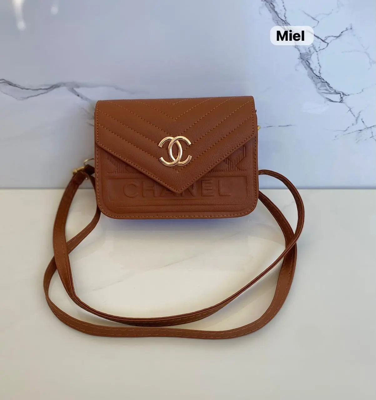 Cartera marrón "Miel" tipo Chanel con logo dorado, relieve "CHANEL" y correa cruzada.