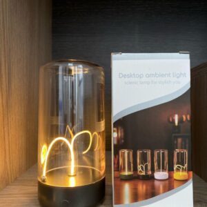 Lámpara táctil imantada de sobremesa con cuerpo de vidrio cilíndrico y filamento luminoso curvo, junto a su caja de empaque con diseño decorativo.